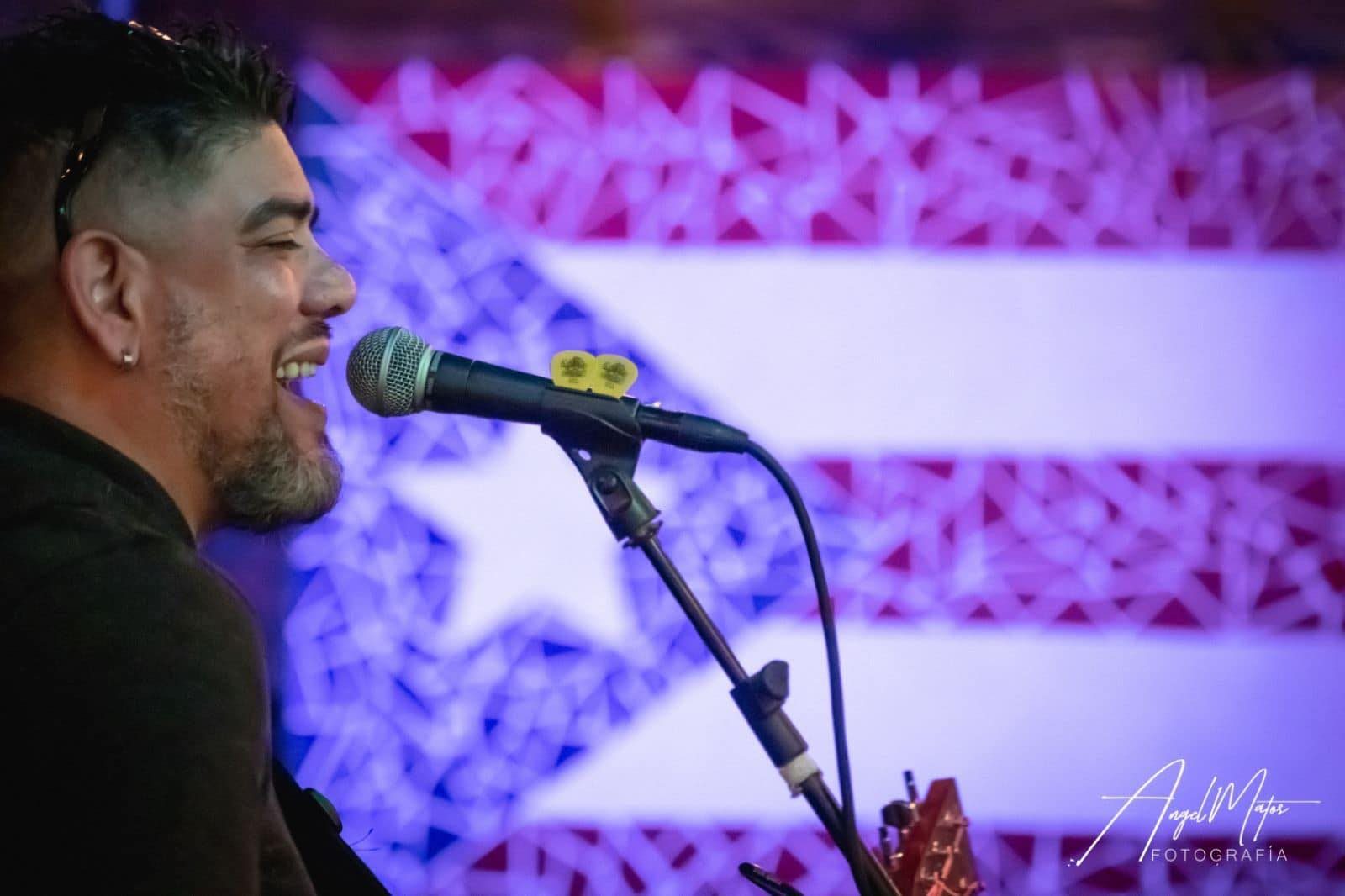 Sammy Vélez singing in front of a Puerto Rican flag