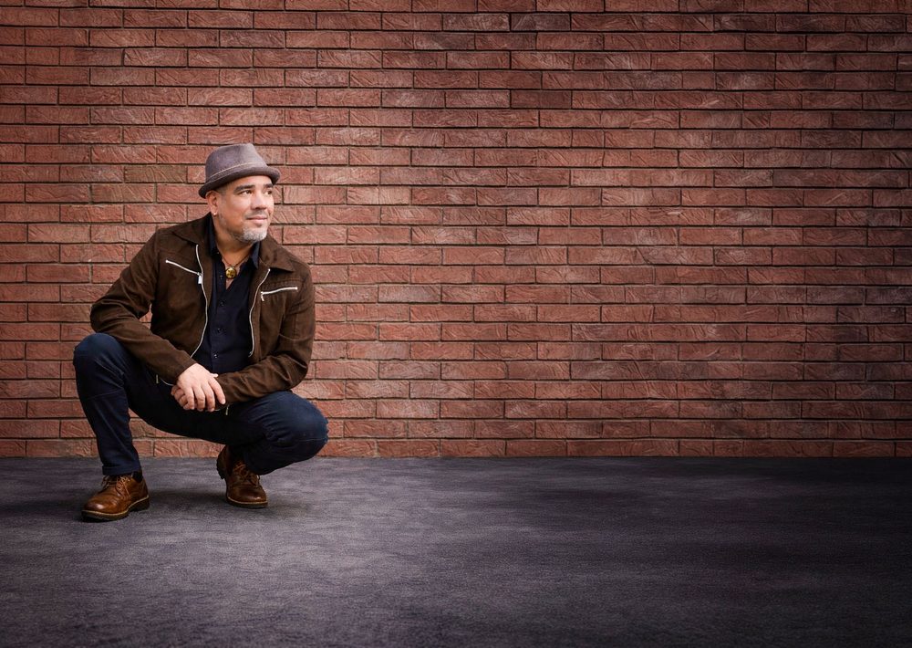 Sammy Vélez crouching by a brick wall
